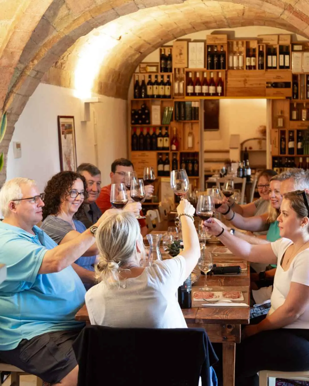 The interior of the Fattoria San Michele a Torri. The image shows people around a wooden table, having a wine tasting. They are all having a toast. 